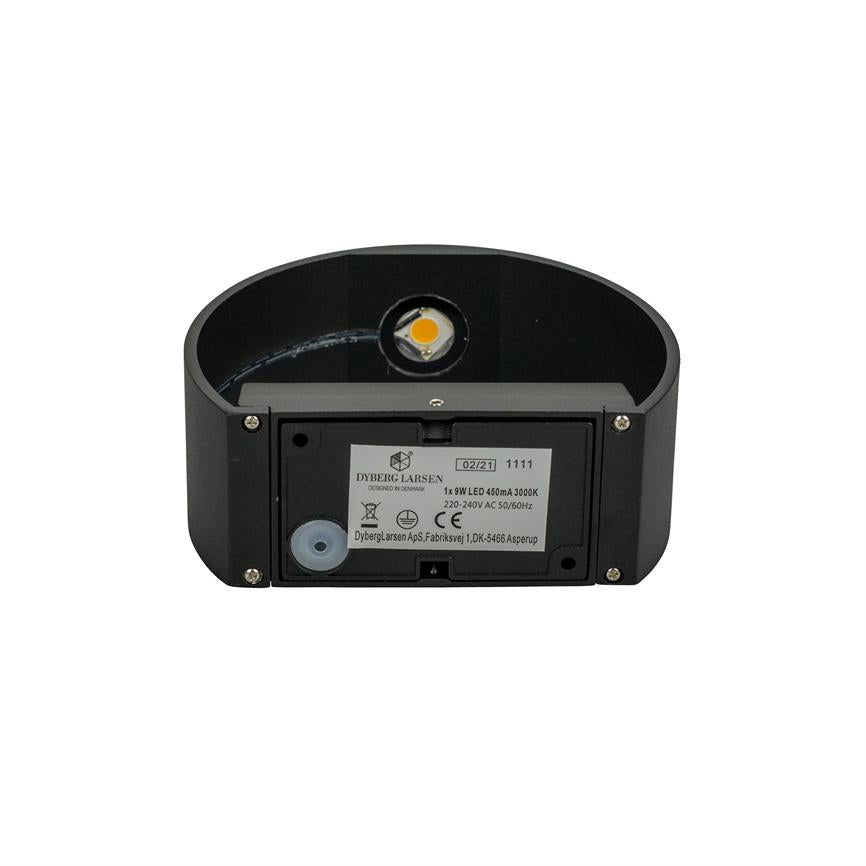 Black oval wall lamp shows open back with visible LED module and mounting sticker, placed against white background.
 
 Transcribed text:
 DYBERG LARSEN
 DESIGNED IN DENMARK
 02/21 1111
 1x 9W LED 450mA 3000K
 220-240V AC 50/60Hz
 CE
 DybergLarsen ApS, Fabriksvej 1, DK-5466 Asperup