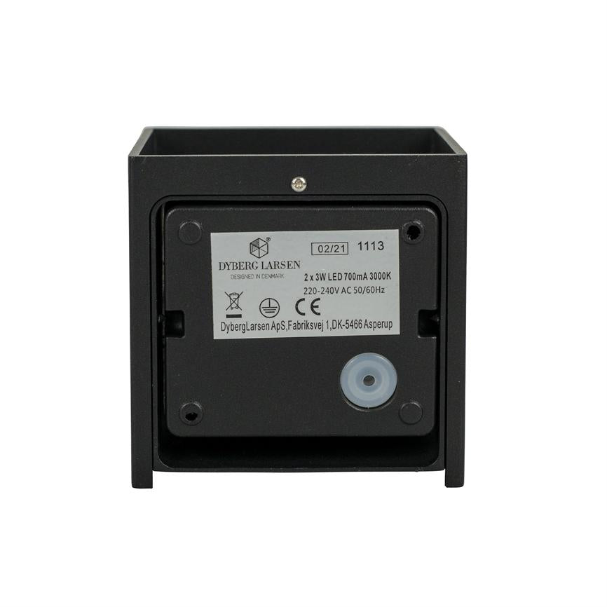 A square black LED fixture shows its backside; label, screws and a round rubber cable gland are visible against a uniform white background.
 
 Text on the label:
 DYBERG LARSEN
 DESIGNED IN DENMARK
 02/21 1113
 2 x 3W LED 700mA 3000K
 220-240V AC 50/60Hz
 DybergLarsen ApS, Fabriksvej 1, DK-5466 Asperup