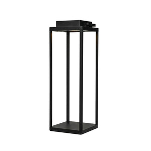A tall, black metal lantern stands free-standing; its four slender columns enclose an open center, with a built-in light source at the top, set against a clean, white background.