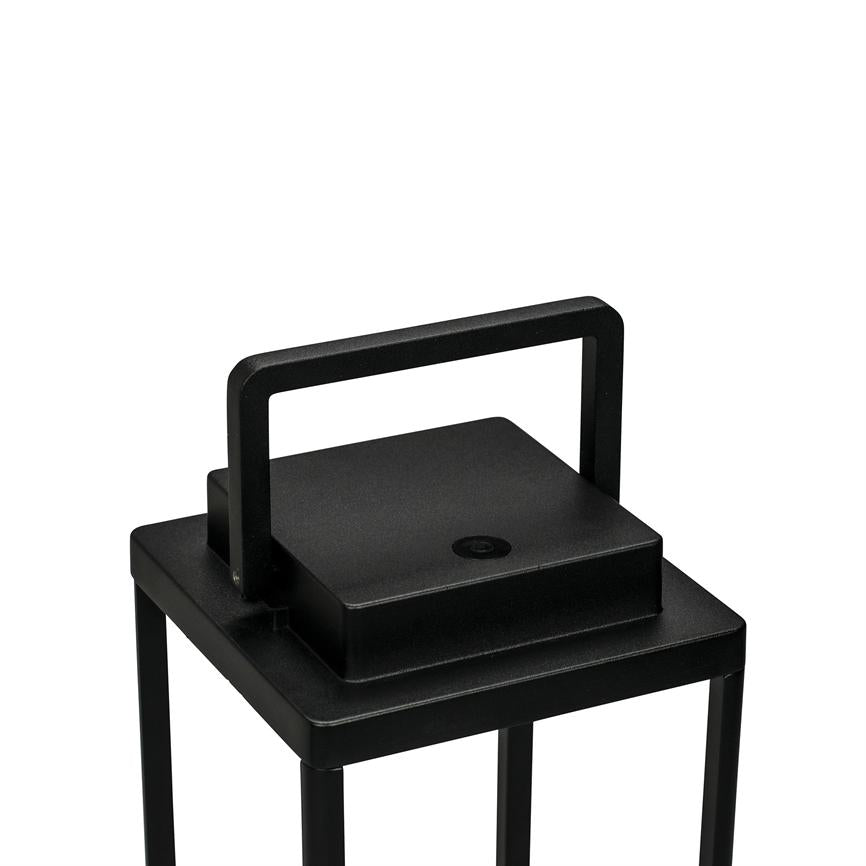 Black, square metal lantern with rectangular upright handle, placed on slender legs; the top shows a small round button, photographed against a solid white background.