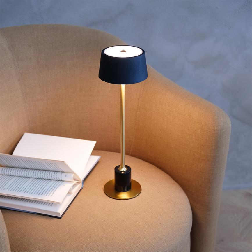 Table lamp casts warm light over an open book, placed on the seat of a beige upholstered armchair in a neutral, muted room.