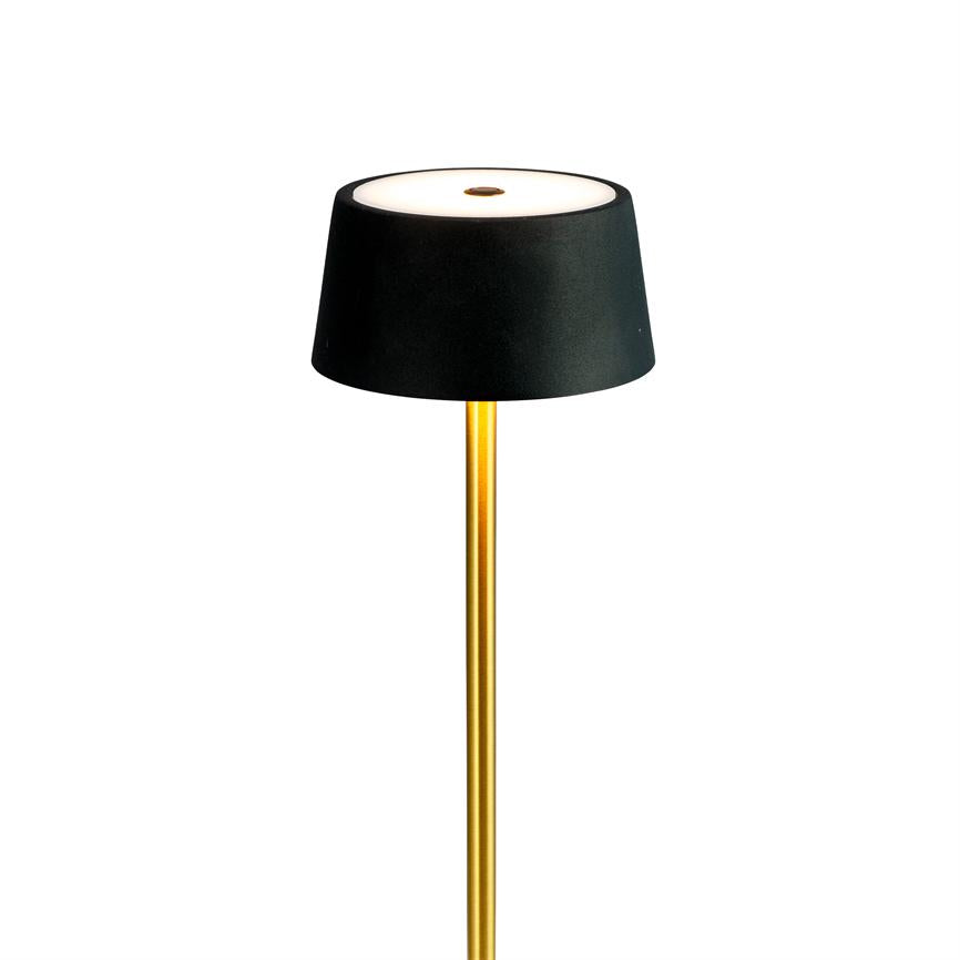 Floor lamp with black shade, which emits a soft white light from its top; slender gold colored bar, set against a uniform white background.