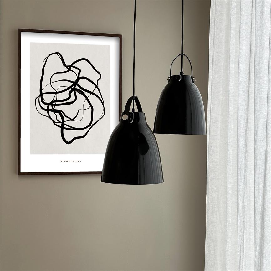 Two black lamps hang in front of a wall poster with black abstract lines; the poster has the text "STUDIO LINES" at the bottom; light curtains on the right in a neutral room.