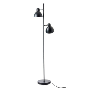 Sort metal gulvlampe med to justerbare skærme monteret på en slank stang over rund fod; skærmene peger nedad og skråt, placeret på hvid studiebaggrund, ledning synlig.