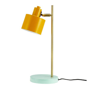 Yellow table lamp with slanted shade, mounted on a slender brass rod and mint green round base; black wire runs out to the side on white background.