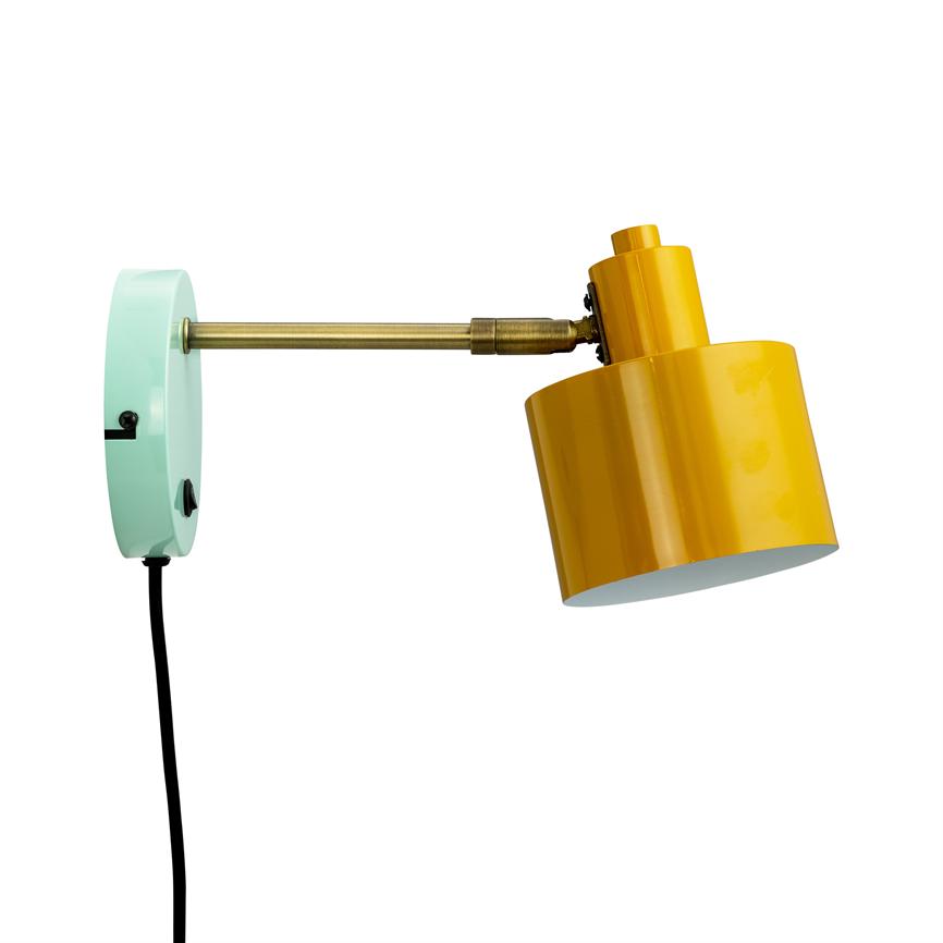 Wall lamp with yellow metal shade mounted on mint green wall bracket, brass arm, cord hanging down; the screen is angled obliquely downwards against a neutral white background.