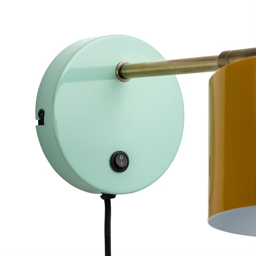 Round mint green wall-mounted lamp base with metal arm extending to right holding yellow shade over white background; black fabric cord downwards. Interrupts the mark 'I' and 'O'.