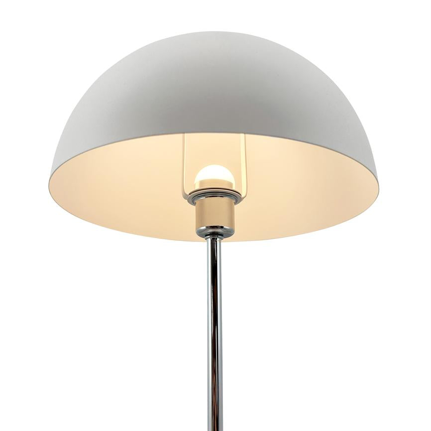 Table lamp with hemispherical, white shade radiates warm light; the bulb is visible in the center and mounted on a shiny chrome rod in front of a neutral white background.