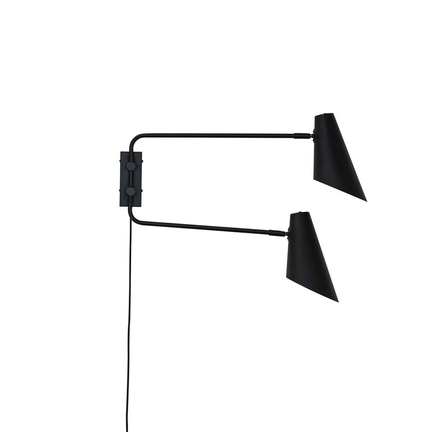 Black wall lamp with two adjustable arms; each arm holds a black conical shield pointing right. Mounted on a vertical wall plate, black wire hangs down towards the floor.