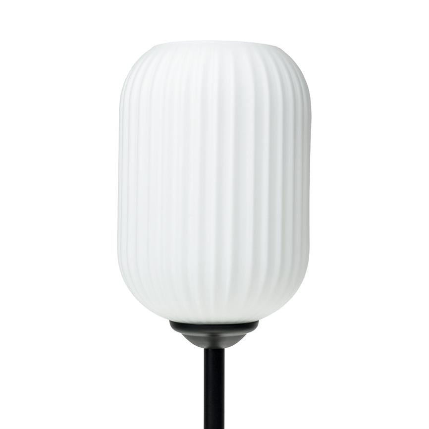 A white fluted glass lampshade mounted on a black metal rod against a neutral white background; cylindrical with rounded ends and vertical grooves, not lit.