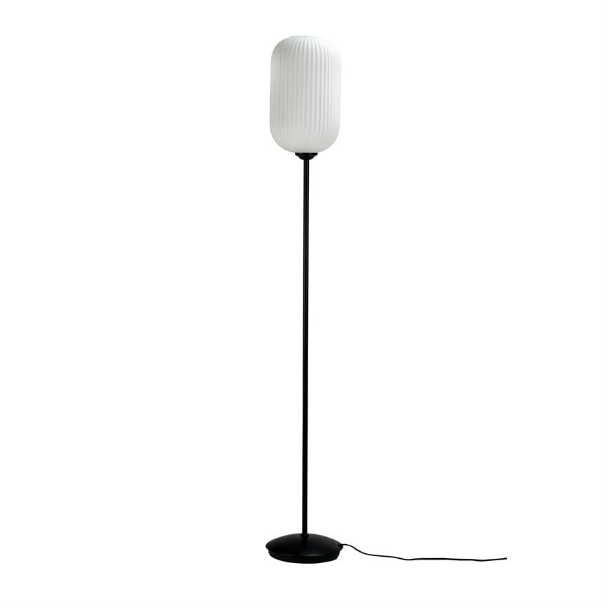 Floor lamp stands upright against a white background; a slender black bar and flat round foot support a white, vertically grooved, oval shade, with a loose black cord.