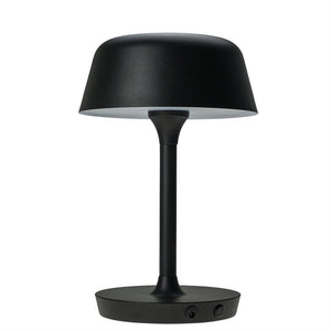 Black table lamp with round shade on slim central pole; stands on a flat, round base, functional table design in a modern, minimalist style in front of a white, uniform background.