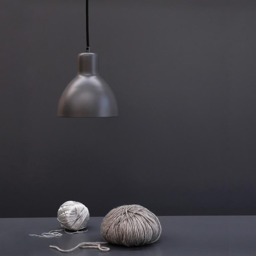 A matte gray ceiling lamp hangs above two gray twine keys that lie on a dark gray table in a minimalist, monochromatic gray room.