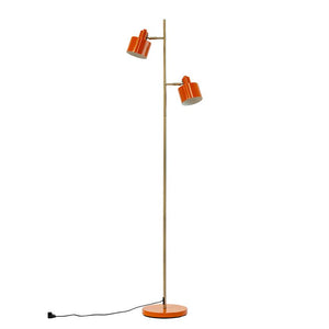 Gulvlampe med to orange lamper monteret på en slank messingstang; står på rund orange fod, skærme vinklet udad, sort ledning ligger mod hvid baggrund.