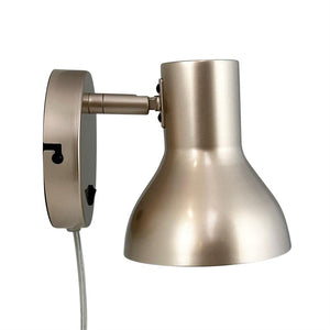 Metallic wall lamp with rounded shade pointing downwards; short hinged arm connects the screen to a round wall base, and a transparent power cord hangs down against a uniform white background.