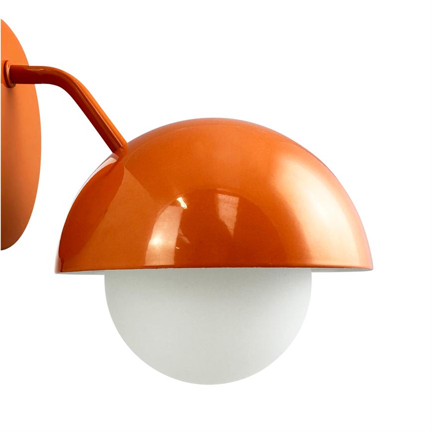 An orange wall lamp is mounted on a short, curved arm; a glossy hemispherical shade embraces a white glass globe, set against a neutral white background.