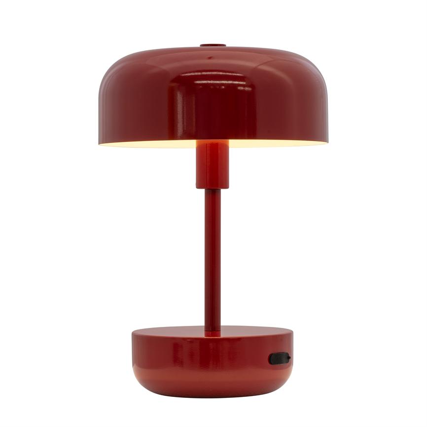 Table lamp in red, modern design; lit and casts warm, downward light; cylindrical stem connects round base and domed shade; placed against a neutral, white background.