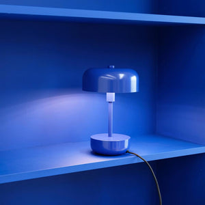 Table lamp is lit on a blue shelf in a built-in blue niche, casting soft light on the wall; a black wire runs over the edge of the shelf.