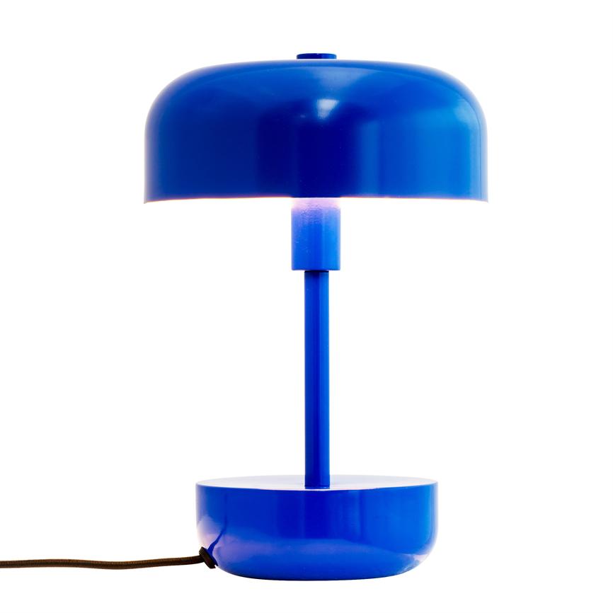 Blue, round table lamp glows dimly between screen and column; cylindrical rod connects top and bottom bowls, set against white background with black fabric cord to left.