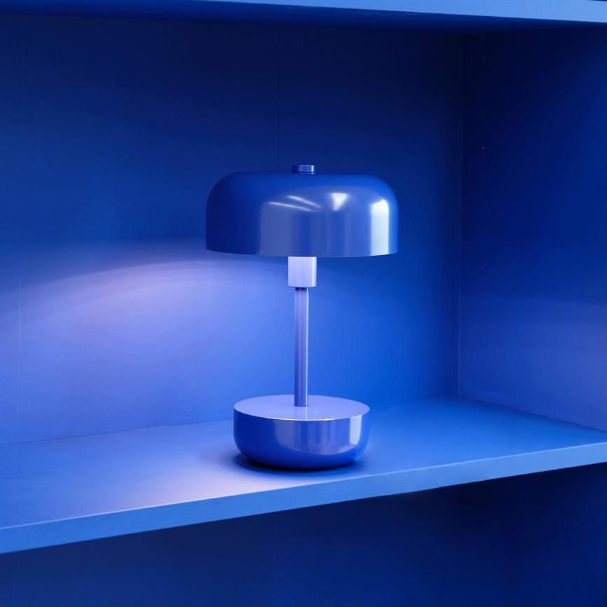 Table lamp is lit on a blue shelf in a framed niche; the round screen casts soft light and surrounds the environment in intense cobalt blue.