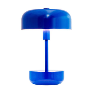 A blue table lamp with round shade and base, emits white light through the space between the shade and base, placed against a clean, white background.