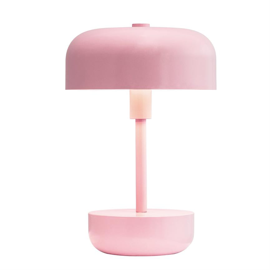 Lampe står tændt på en rund base og udsender blødt nedadrettet lys gennem en mat lyserød kuppel; minimalistisk design mod hvid baggrund.