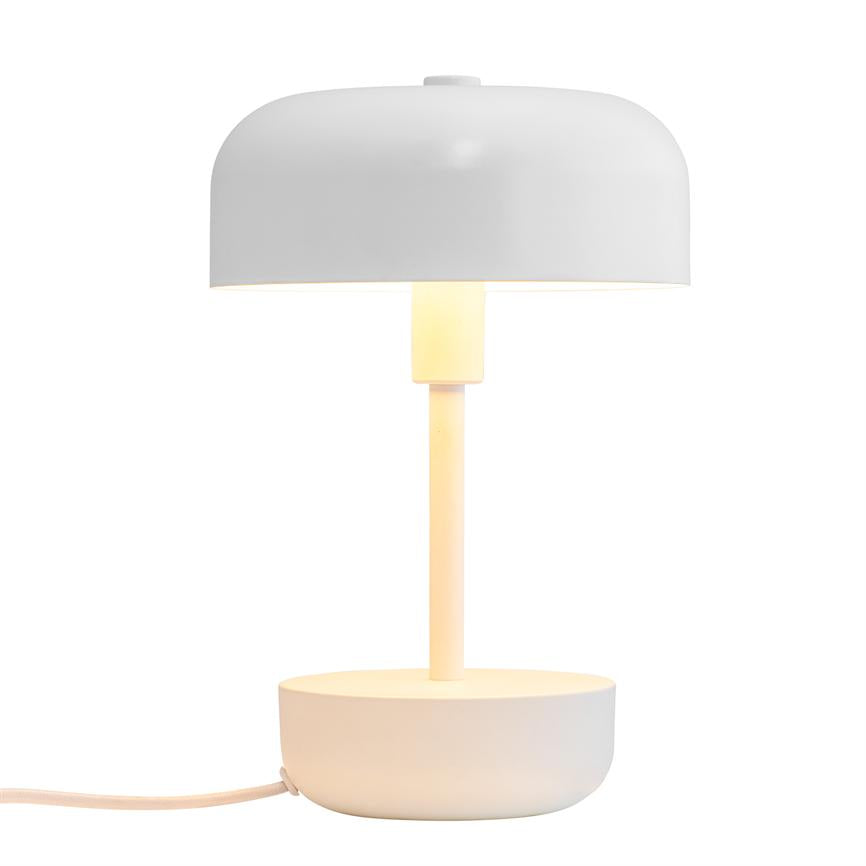 A white table lamp emits warm light; a slim bar connects a round bowl-shaped base to a wide, curved shade on a neutral white background.