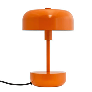 An orange metal table lamp stands on a white background: round dome, narrow column, cylindrical base and round foot, with black power cord running out to the left.