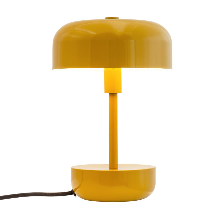 Yellow table lamp with dome-shaped shade, vertical shaft and round base; the lamp is on, casts light downwards and has a visible black cord against a white studio background.