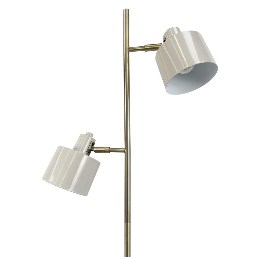 Floor lamp with two white metal shades, each angled differently; they are mounted on a slender antique brass rod in front of a uniform white background.