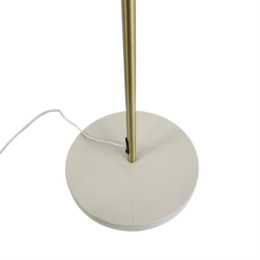Round white lamp base carries a vertical brass colored rod; a white cord with a black on/off button lies twisted across the base on a white background.