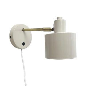 Wall lamp mounted on round wall plate; lamp head hangs from a short brass arm and points downwards; white lacquered cylindrical screen, small black on/off button and white fabric cord.