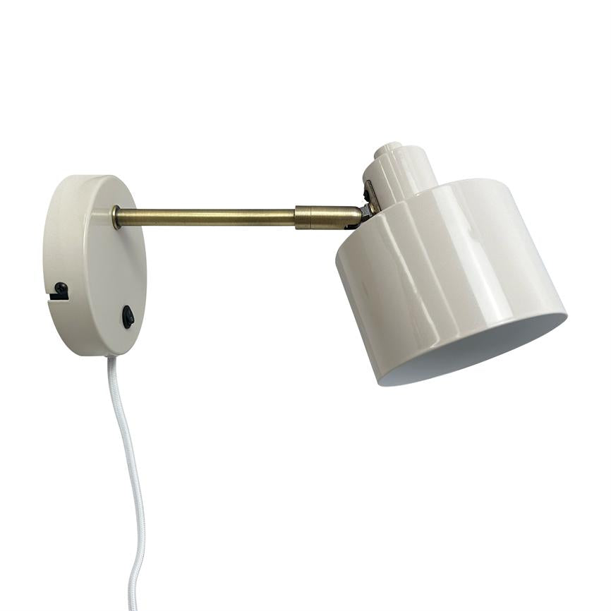 Wall lamp with white cylindrical lampshade, angled downwards; mounted on round white wall bracket with short brass arm and white textile cord against white background.
