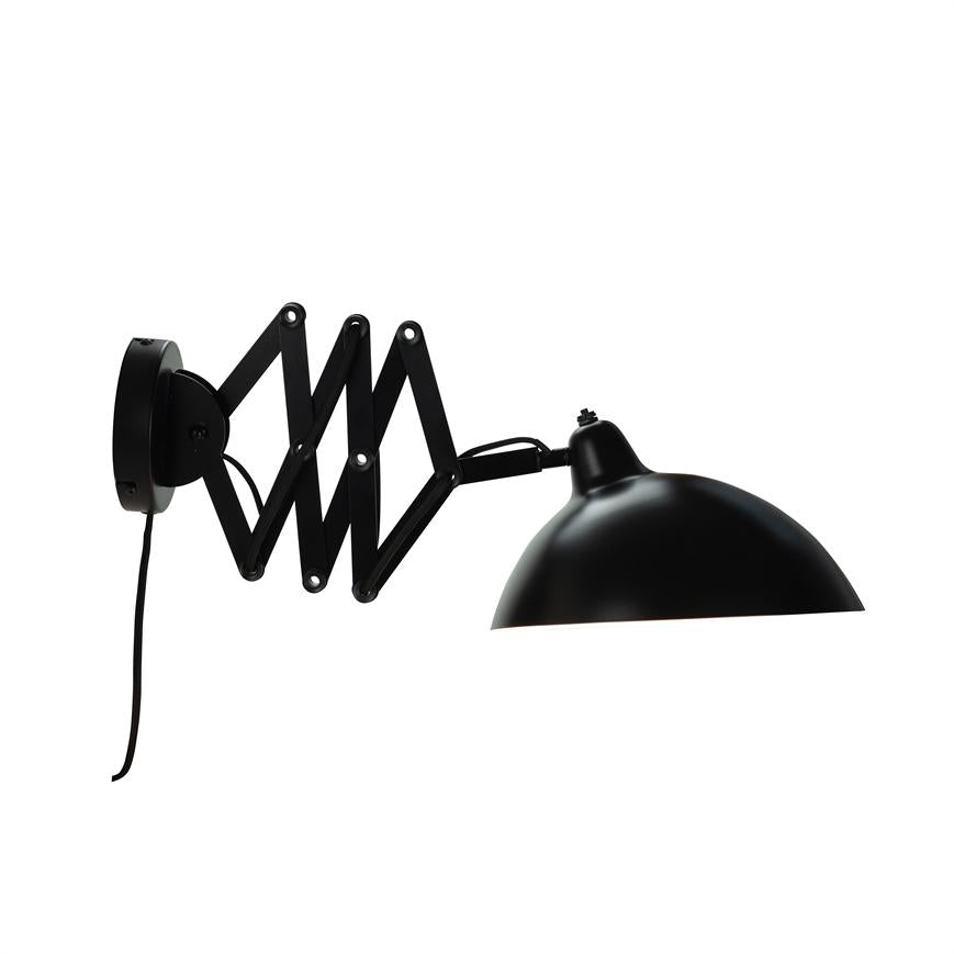 Black wall lamp with hemispherical shade, extended on a folding scissor arm; arm and screen pointing right against pure white background, a black cable hanging down.