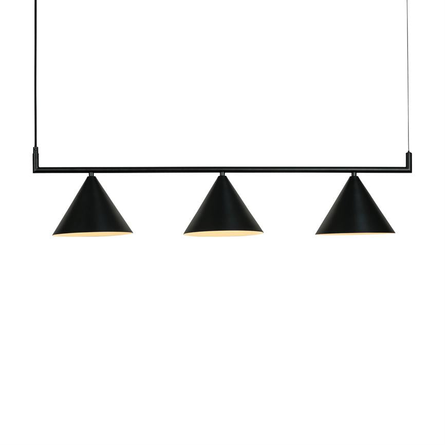 Three black, conical pendant lamps hang from a black rod via thin cables, emitting warm light, in a clean, white, minimalist room.