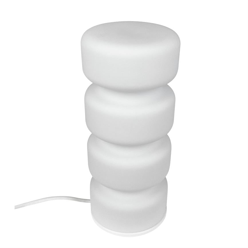 White table lamp stands upright — four stacked, soft round segments; on white background with a thin power cable running out to the left.