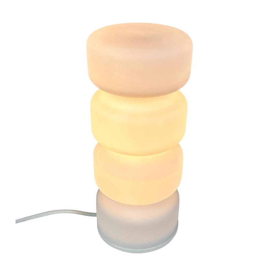 Table lamp consisting of four stacked, matt cylindrical discs; two middle discs emit warm, yellowish glow. Placed against a white background with a visible white wire on the left.