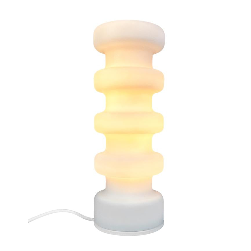 Table lamp with stack of wide, rounded discs glows warmly; it stands on a round base with white cord visible against a uniform white background, in a minimalist environment.