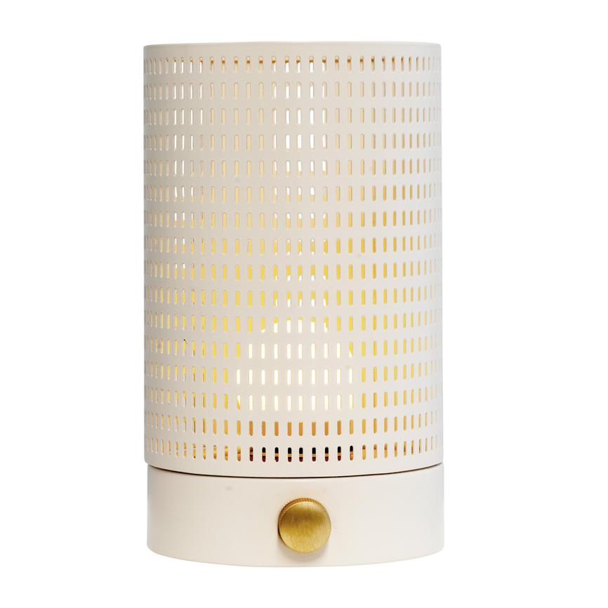 Cylindrical table lamp with white perforated metal casing; warm light shines through rectangular holes, mounted on matt white base with round, brass-coloured knob, set against white background.