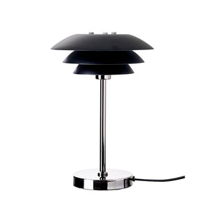 Table lamp with three layered, black shades stands on a chrome rod; round chrome foot and black cord on the right on a neutral white background.