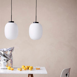 Two white pendant lamps hang above a marble table on which lie yellow lemons, a glass of juice and a shiny silver bag, against a light beige wall with a simple chair at the table.