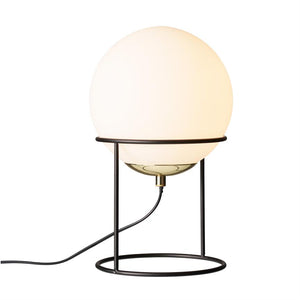 A round opal white glass globe glows warmly, fixed in a black, open metal stand with a circular base; a black wire runs from the bottom of the lamp to the left on a white background.