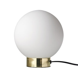 A white globe lamp stands on a polished brass base; a black wire runs out against a neutral white background.