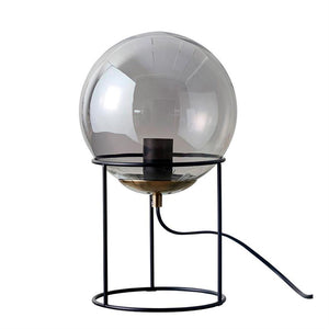 Round smoky glass dome lamp resting in a three-legged black metal stand; socket and black wire visible, placed against a uniform white studio background.