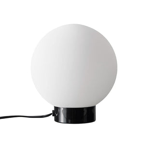 Ball lamp: a large white glass ball sits on a glossy black cylindrical base, with a black cord running out to the side, set against a neutral white background.