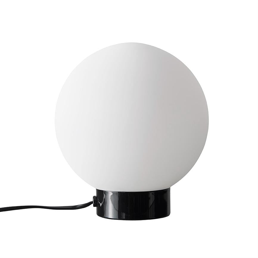 Ball lamp: a large white glass ball sits on a glossy black cylindrical base, with a black cord running out to the side, set against a neutral white background.