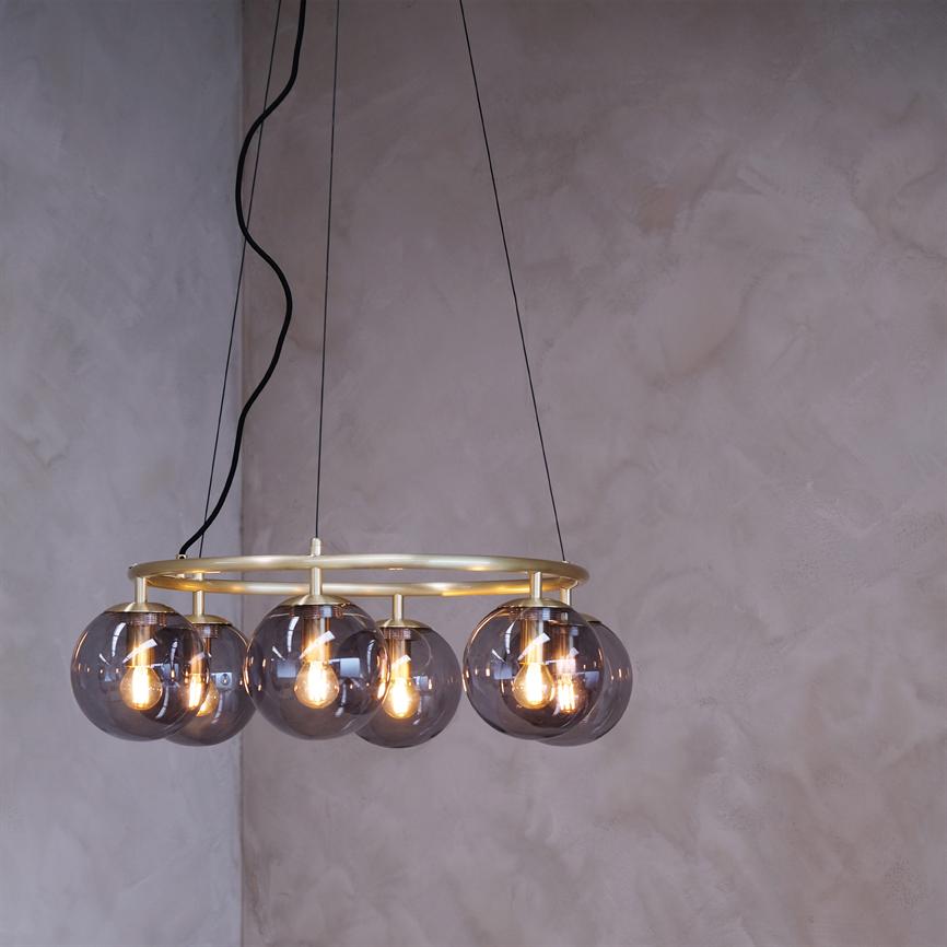 A ring-shaped ceiling lamp with six smoke-colored glass domes hangs and emits warm light in front of a sand-colored, textured wall with exposed wiring.