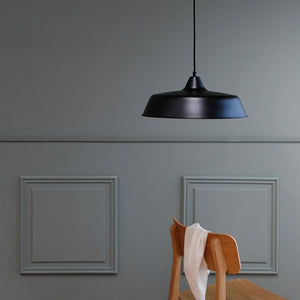 Black metal ceiling lamp hangs above a wooden chair, over which a white piece of fabric is thrown; surrounded by a muted gray wall with two decorative panel frames.