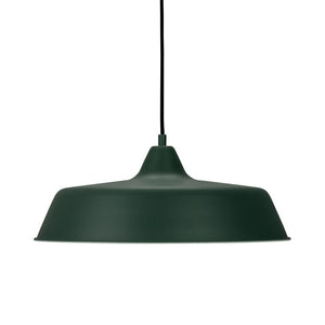 A matte dark green pendant lamp, hangs from a black cord and radiates downward lighting, simple industrial-inspired shape against a neutral white background.