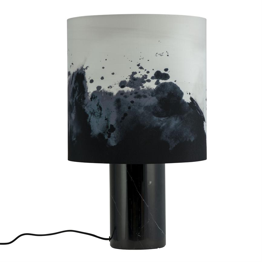 Table lamp with cylindrical black marble base and cylindrical lampshade adorned with black and gray ink spots; cord runs out to the side. Neutral white background.